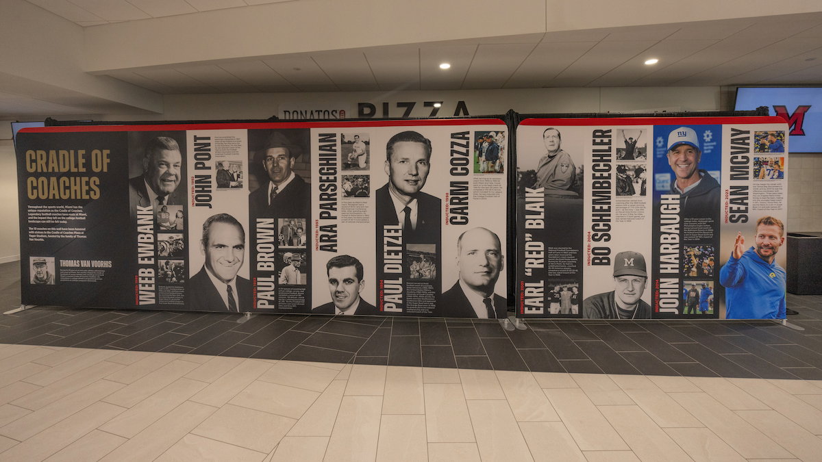 A long display wall features portraits and biographies of prominent football coaches, including Weeb Ewbank, John Pont, Paul Brown, and others, under the title "Cradle of Coaches."